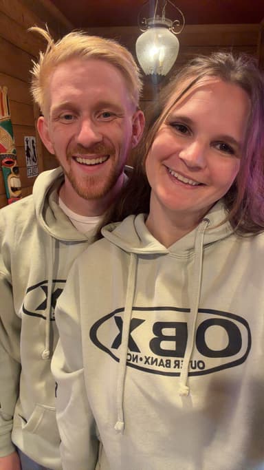 Mel and Scott smiling together in matching Outer Banks sweatshirts