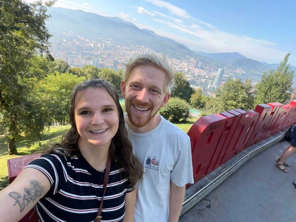 Mel and Scott taking a selfie at a hilltop overlook above a city and mountains