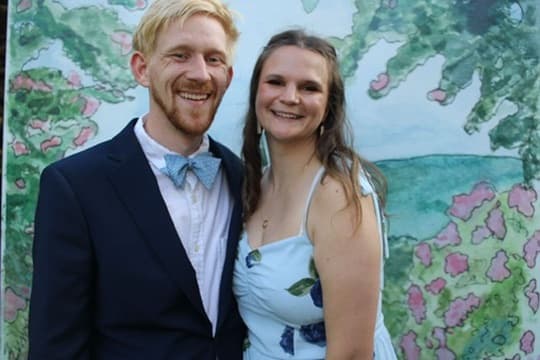 Mel and Scott dressed up, standing in front of a painted floral backdrop